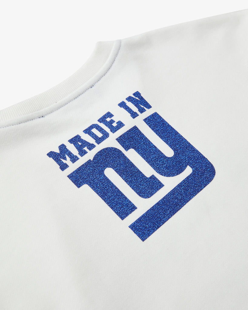 An artistic shot at an angle of the rear of a White Crew Neck , featuring the text Made in NY using the OFFICIAL NFL GIANTS Jersey Font. The Text and graphics all have a shimmering blue color.