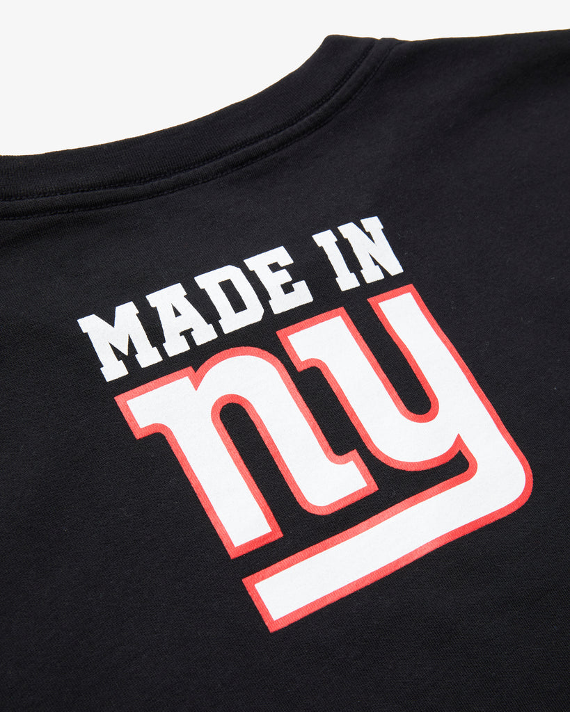 An angled artisitc photo of the rear of a Black Tee Shirt, featuring the text Made in NY using the OFFICIAL NFL GIANTS Jersey Font.